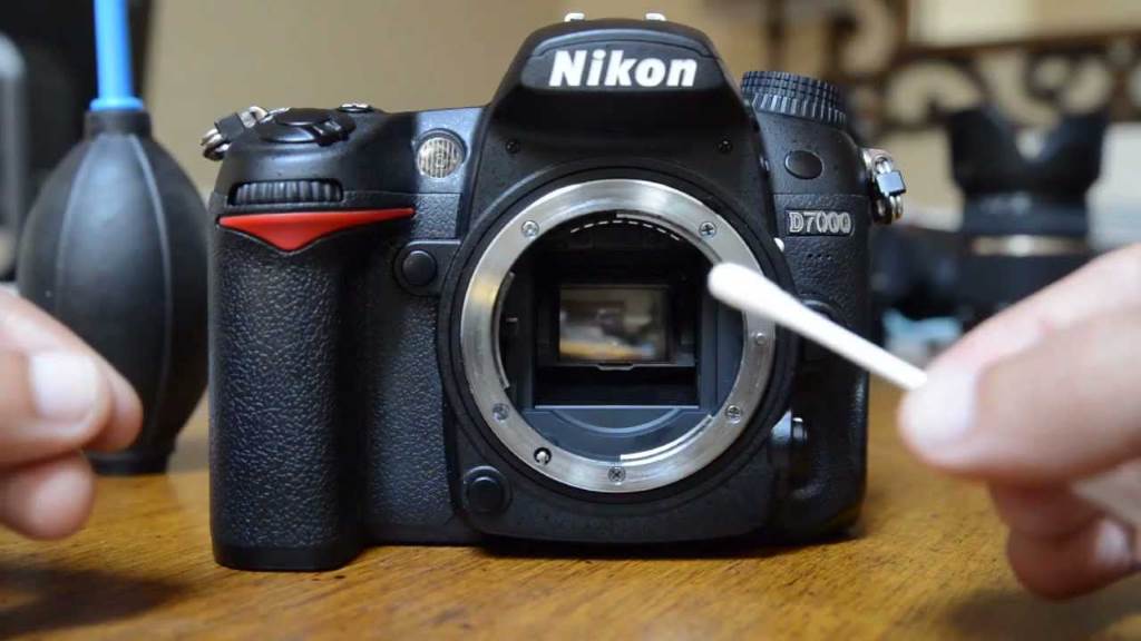 Hands holding a microfiber cloth gently wiping a camera sensor